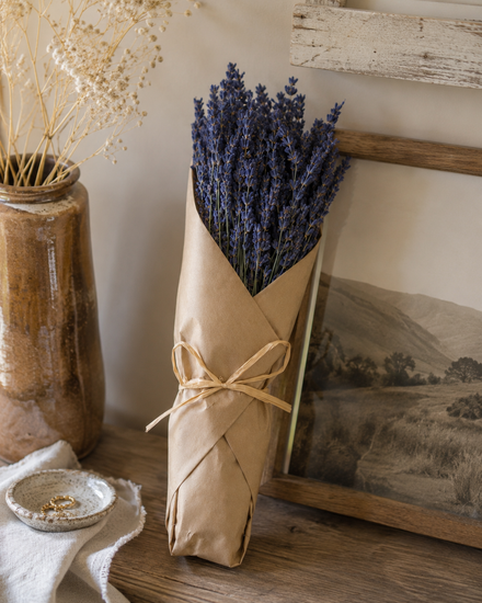 A lavender bunch wrapped in butcher's paper is leaning against a picture frame 